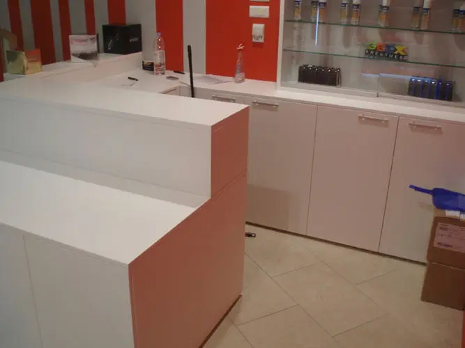 Bijeli prodajni pult i ormarići u trgovini s crvenim zidovima